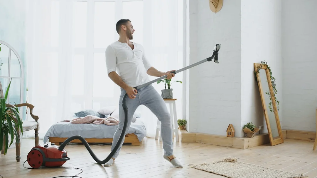 team-01 Une femme adulte en combinaison rouge utilise un aspirateur dans un intérieur moderne, concentrée sur des tâches de nettoyage.