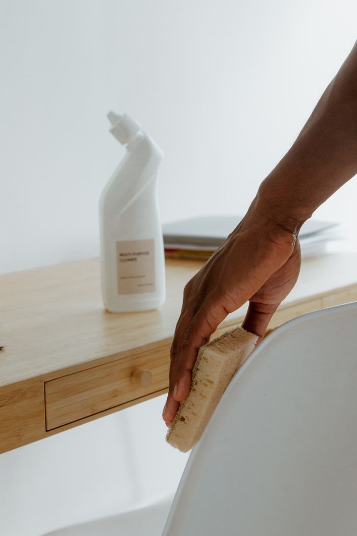 Pièce épurée avec une personne nettoyant une chaise à l'aide d'une éponge et d'un produit d'entretien.